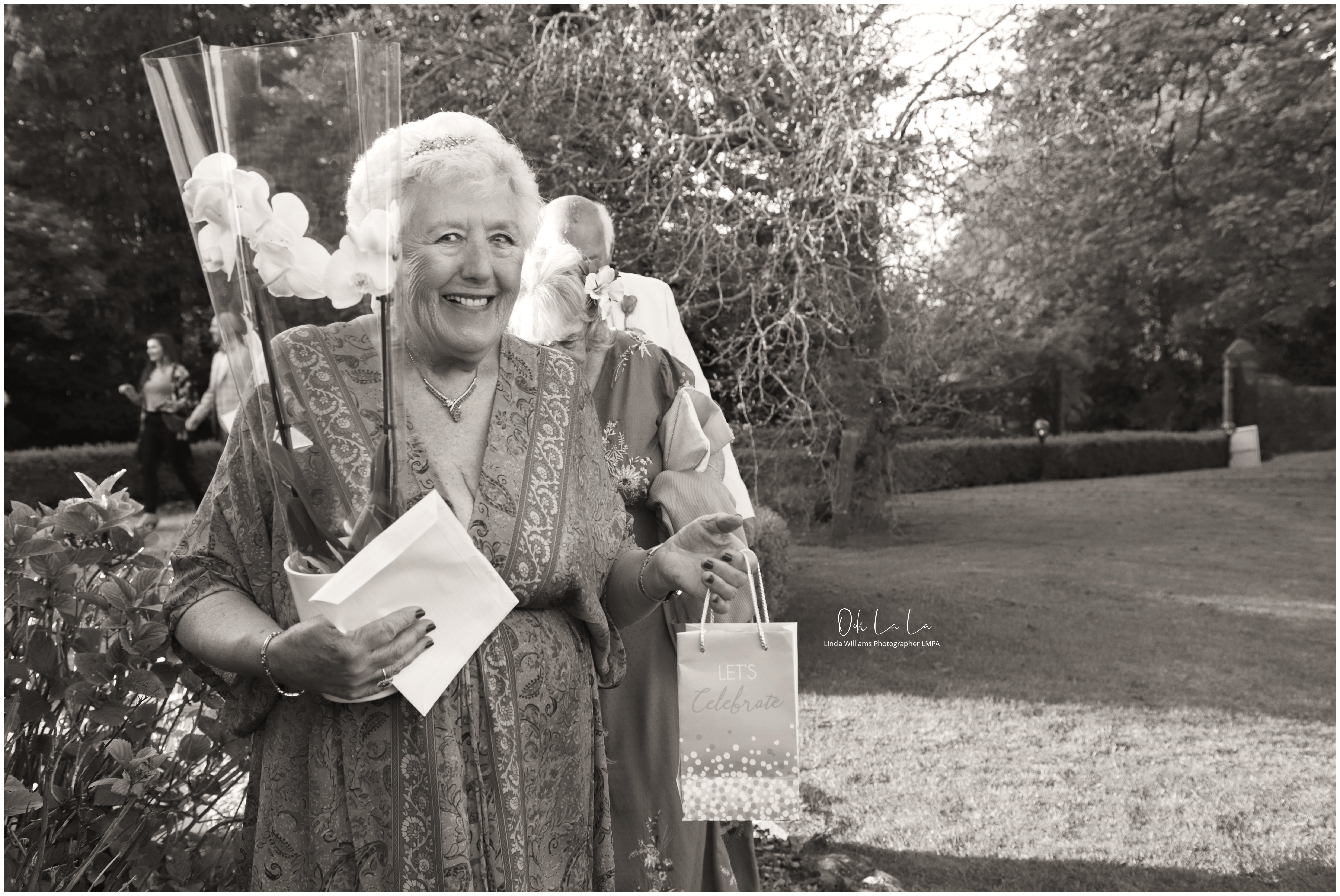black and white shot of lady celebrating her 80th birthday holding gifts and an orchid