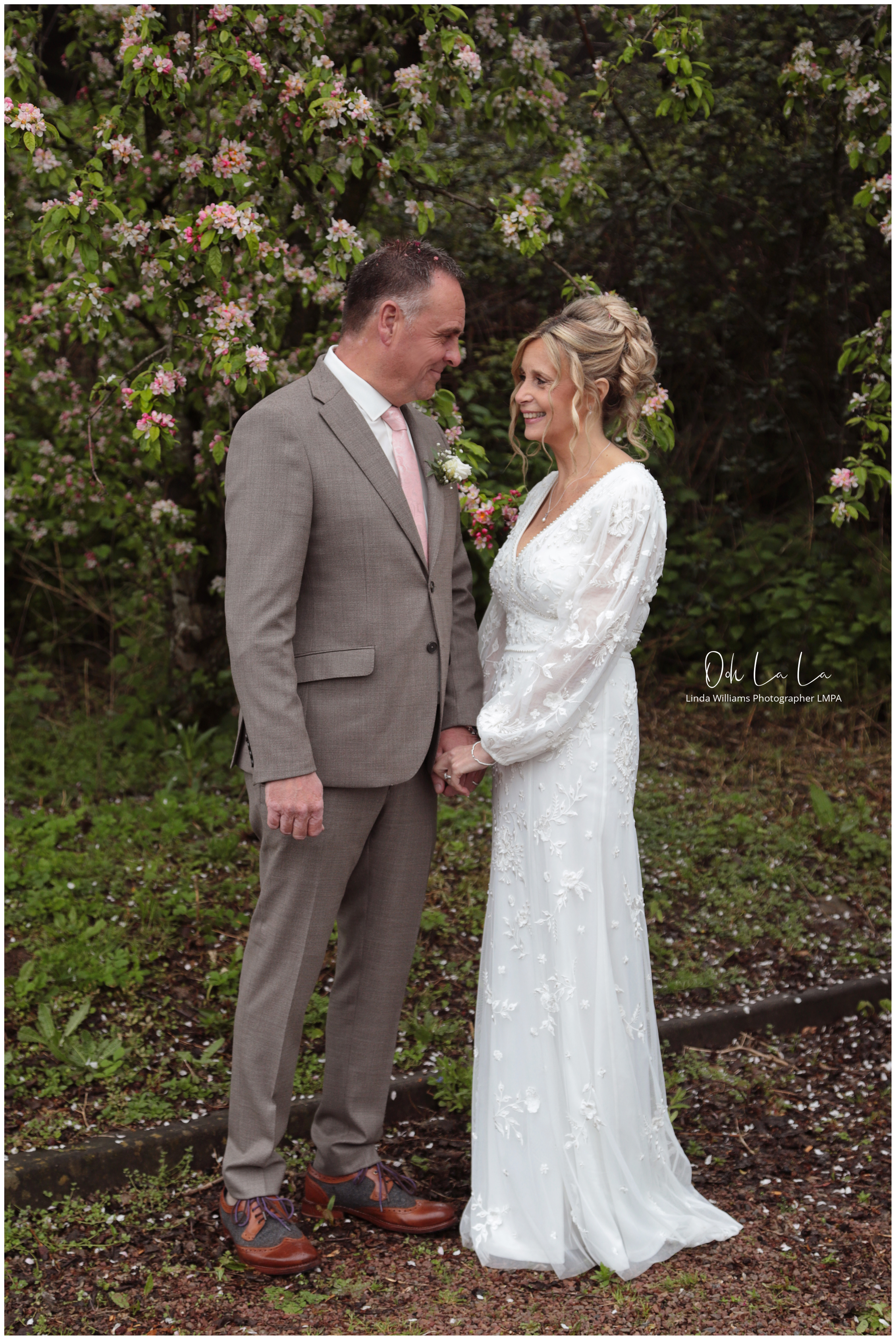 bride and grrom smiling at each other against pink spring blossom