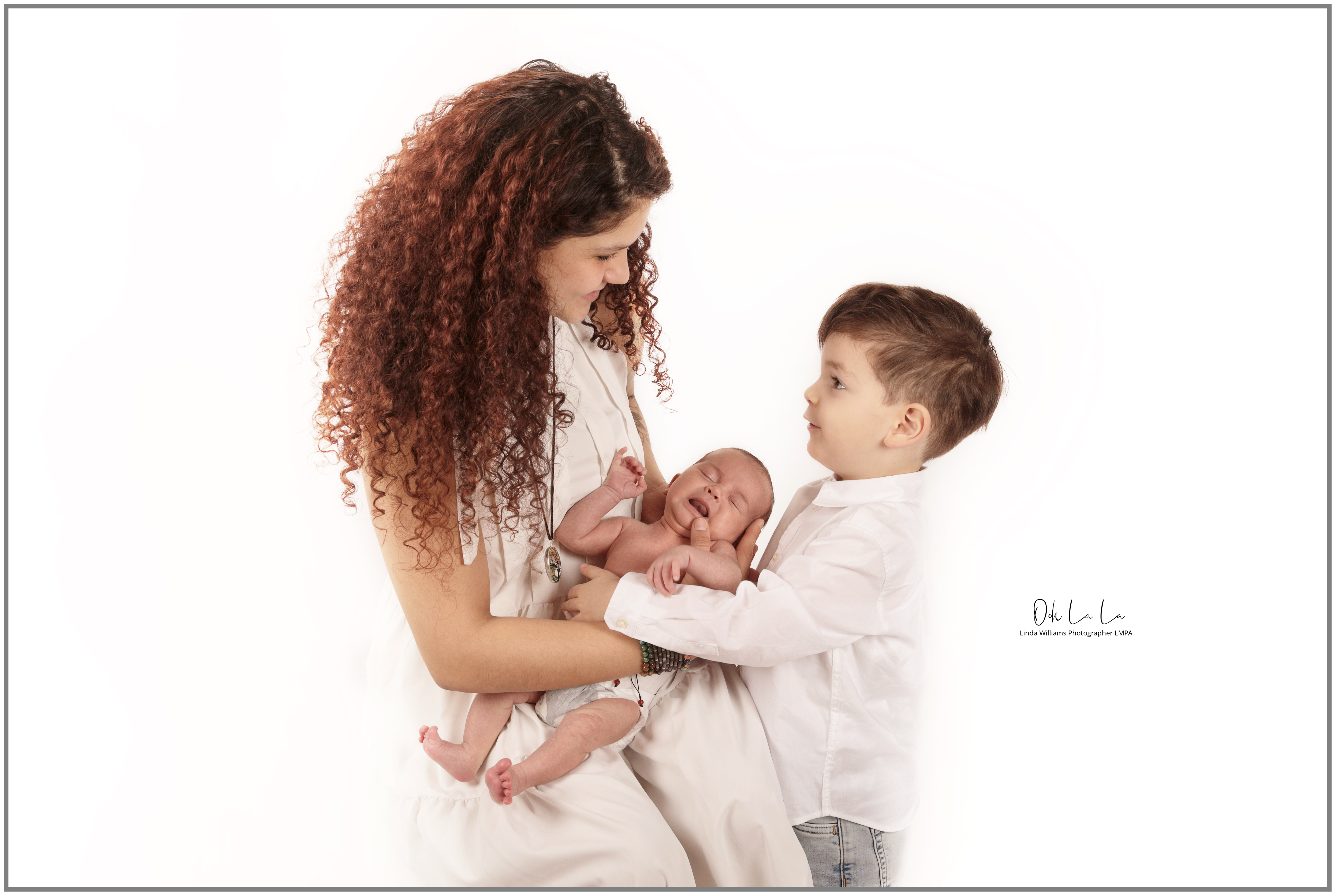 New mother holding crying newborn baby while little boy looks at baby