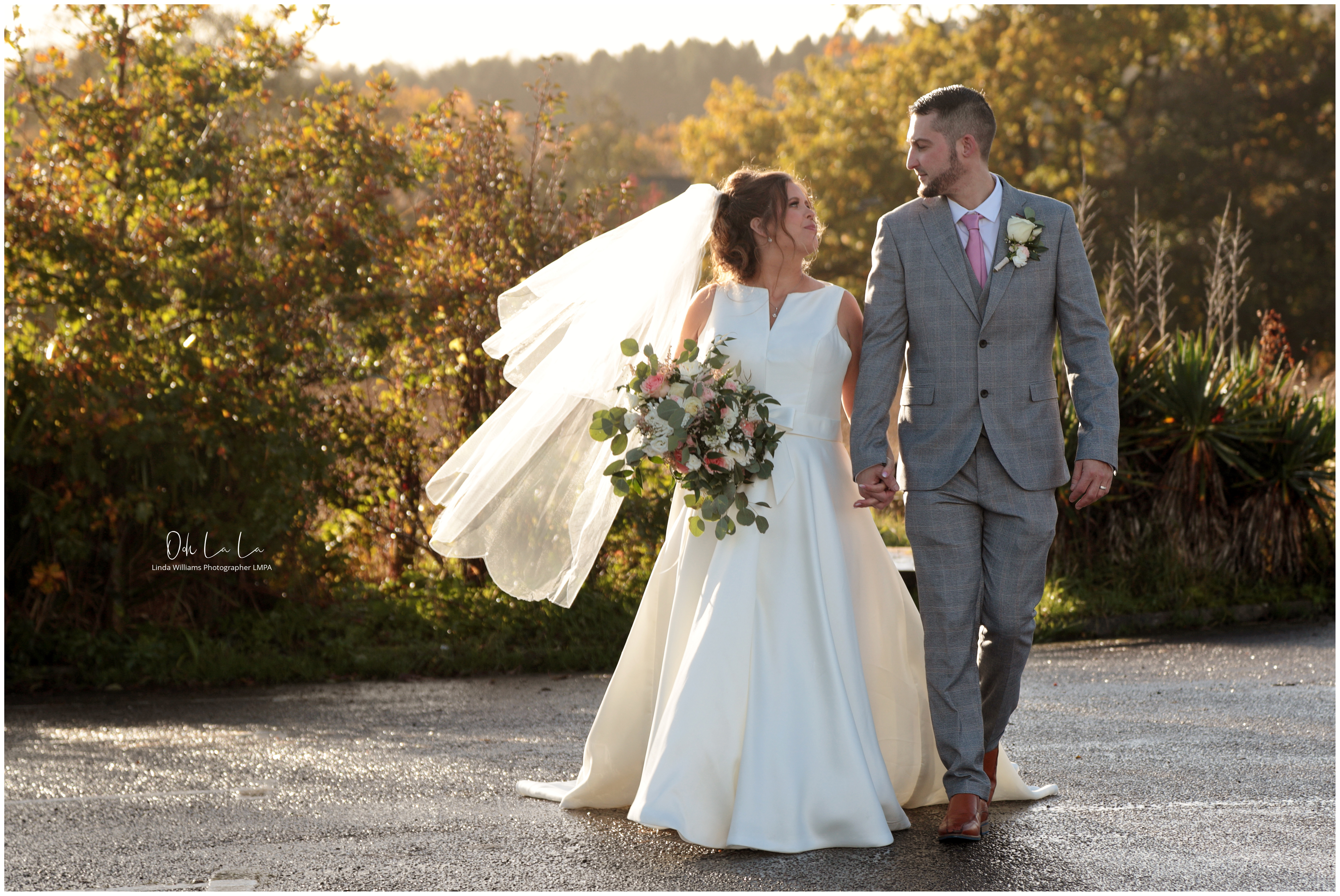 bride and groom walkign together her veil lit up by sunshine